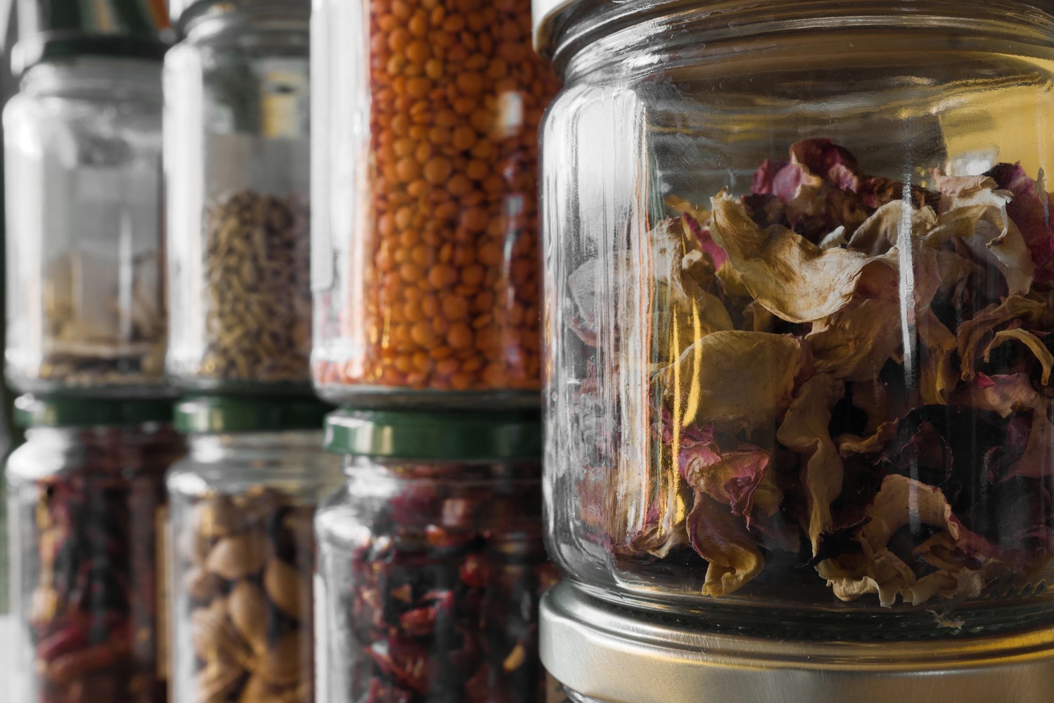 Arrangement of herbs, legumes, and dried rose petals in glasses